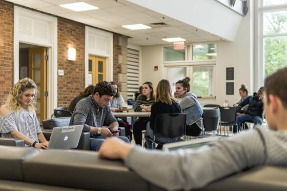 Chatham University students sit in lounge area at tables studying and working on laptops. 