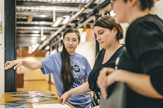 Photo of three people standing in a design lab consulting printed designs. 