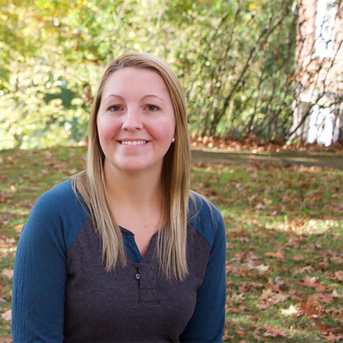 Photo of a young woman with blonde hair and a blue shirt smiling for a photo outside